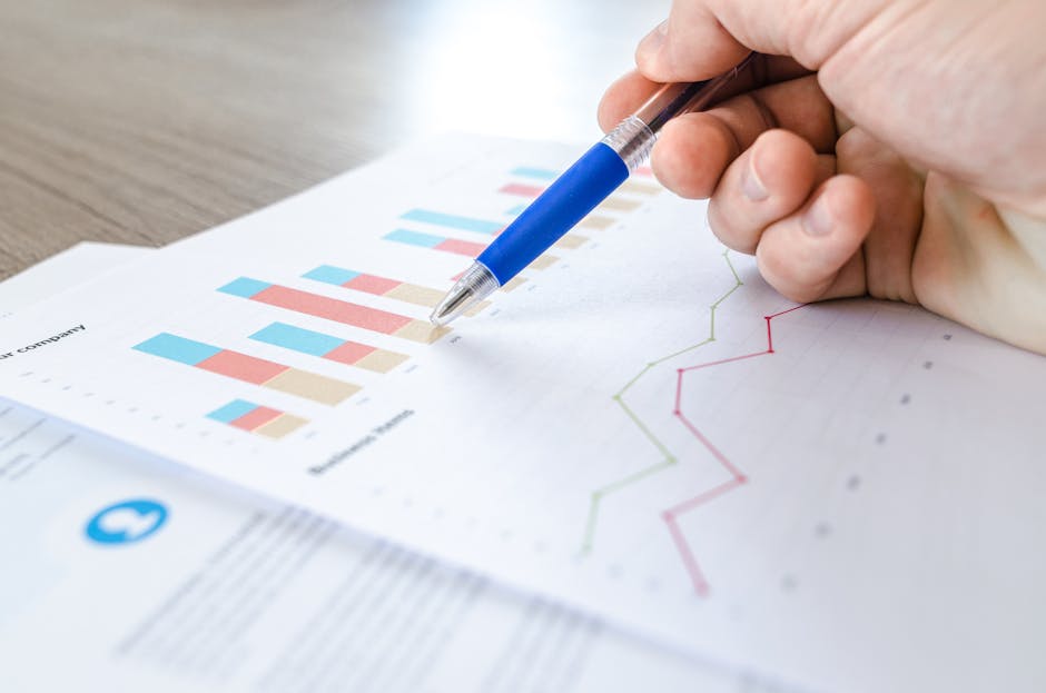 referral program ROI - A close-up of a hand with a pen analyzing data on colorful bar and line charts on paper.