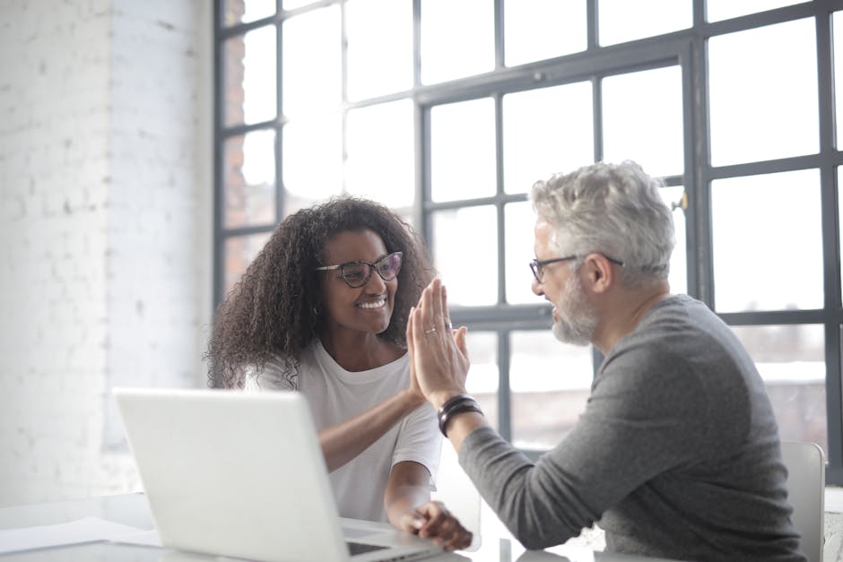 double-sided referral rewards - Side view of cheerful multiracial business partners in informal clothes celebrating successful deal while browsing laptop in spacious coffee shop