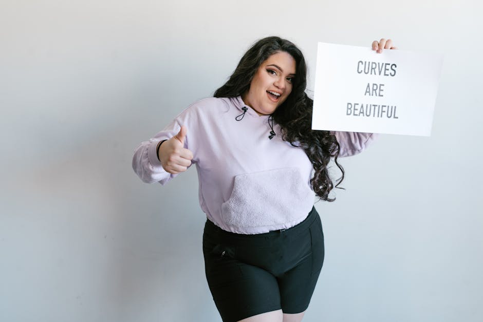 Cheerful plus-size woman holding sign 'Curves Are Beautiful,' promoting self-love.