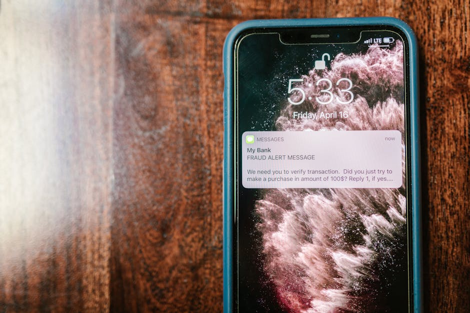 referral fraud prevention - Close-up of a smartphone displaying a fraud alert notification on a wooden surface.