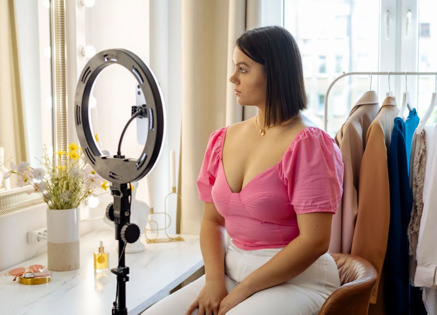 UGC creator program - Young woman in pink top setting up camera for video recording with ring light indoors.