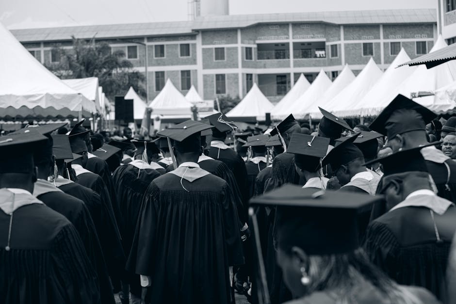 higher education referral marketing - Diverse group of graduates in gowns at an outdoor ceremony with tents and buildings.