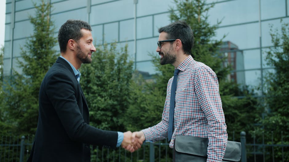 referral marketing news May 2026 - Two men shaking hands outside a modern office building, symbolizing business partnership.