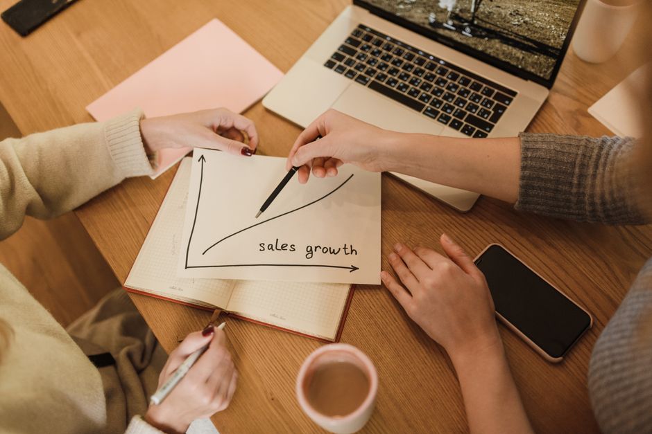 referral and affiliate marketing - Two women plan sales growth with graphs and technology in an office setting.