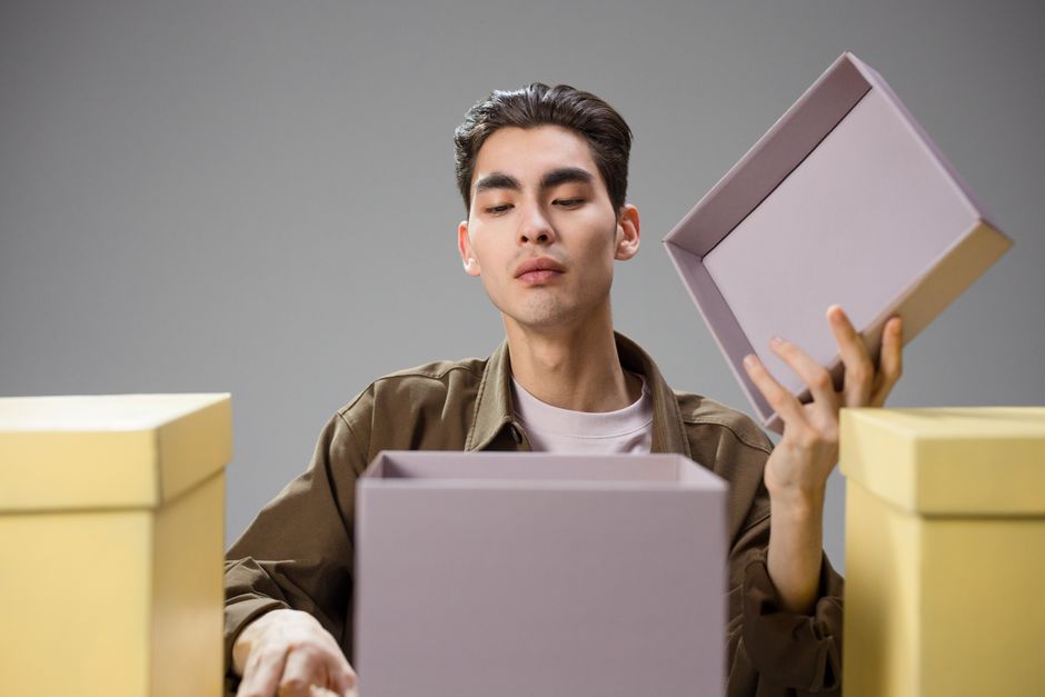 referral marketing examples - Asian man opening a gift box with a curious expression in a studio environment.
