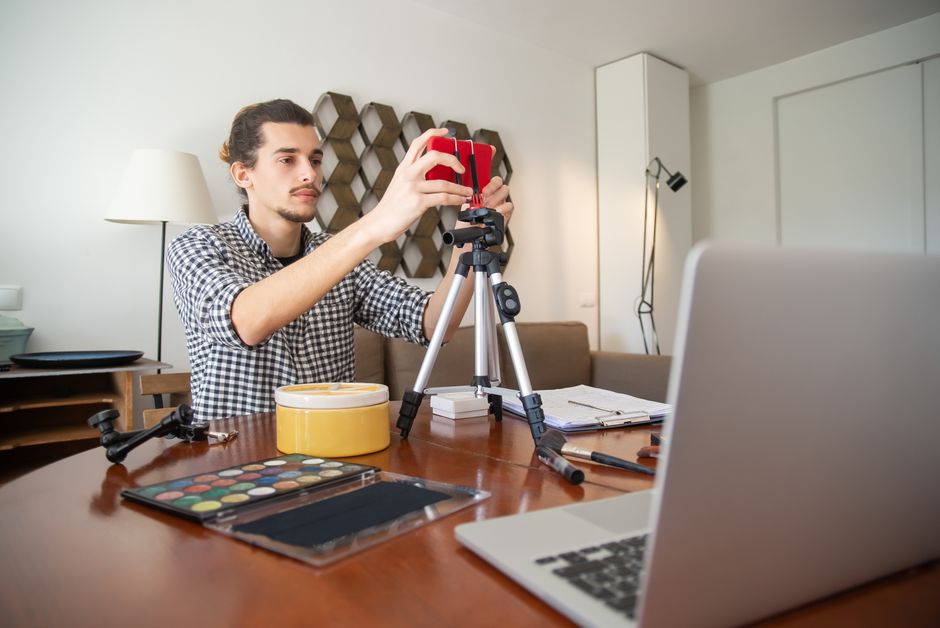 affiliate marketing news - A male vlogger adjusts his camera on a tripod, preparing for a video shoot in a stylish home studio.